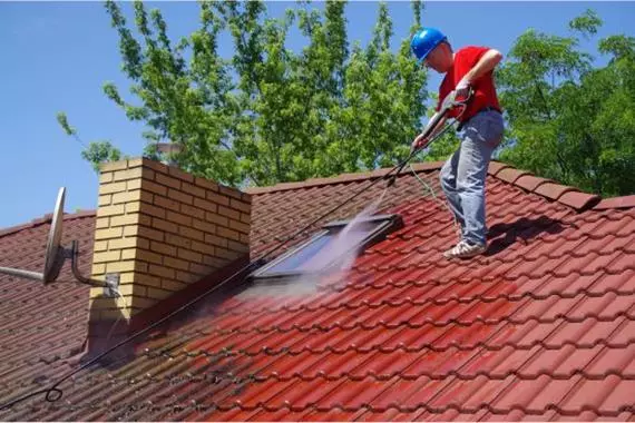 man in helmet pressure washing a red roof